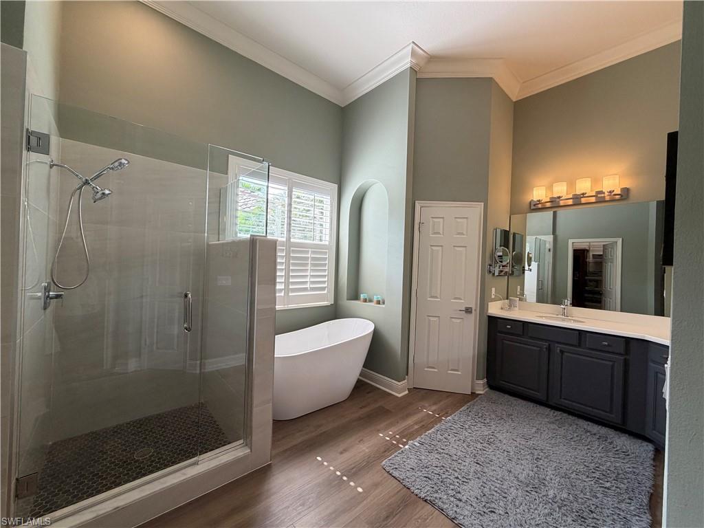 2143 Grove Drive Naples, FL 34120 - Photo 15 of 37 Bathroom with vanity, a stall shower, a freestanding tub, dark wood-style flooring, and ornamental molding
