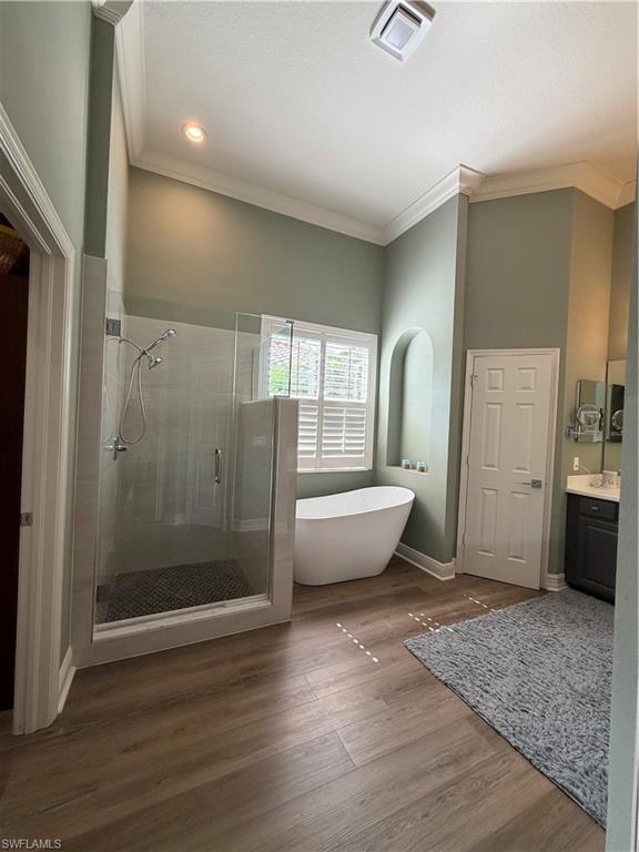 2143 Grove Drive Naples, FL 34120 - Photo 16 of 37 Bathroom with a stall shower, vanity, a freestanding tub, dark wood-style flooring, and ornamental molding