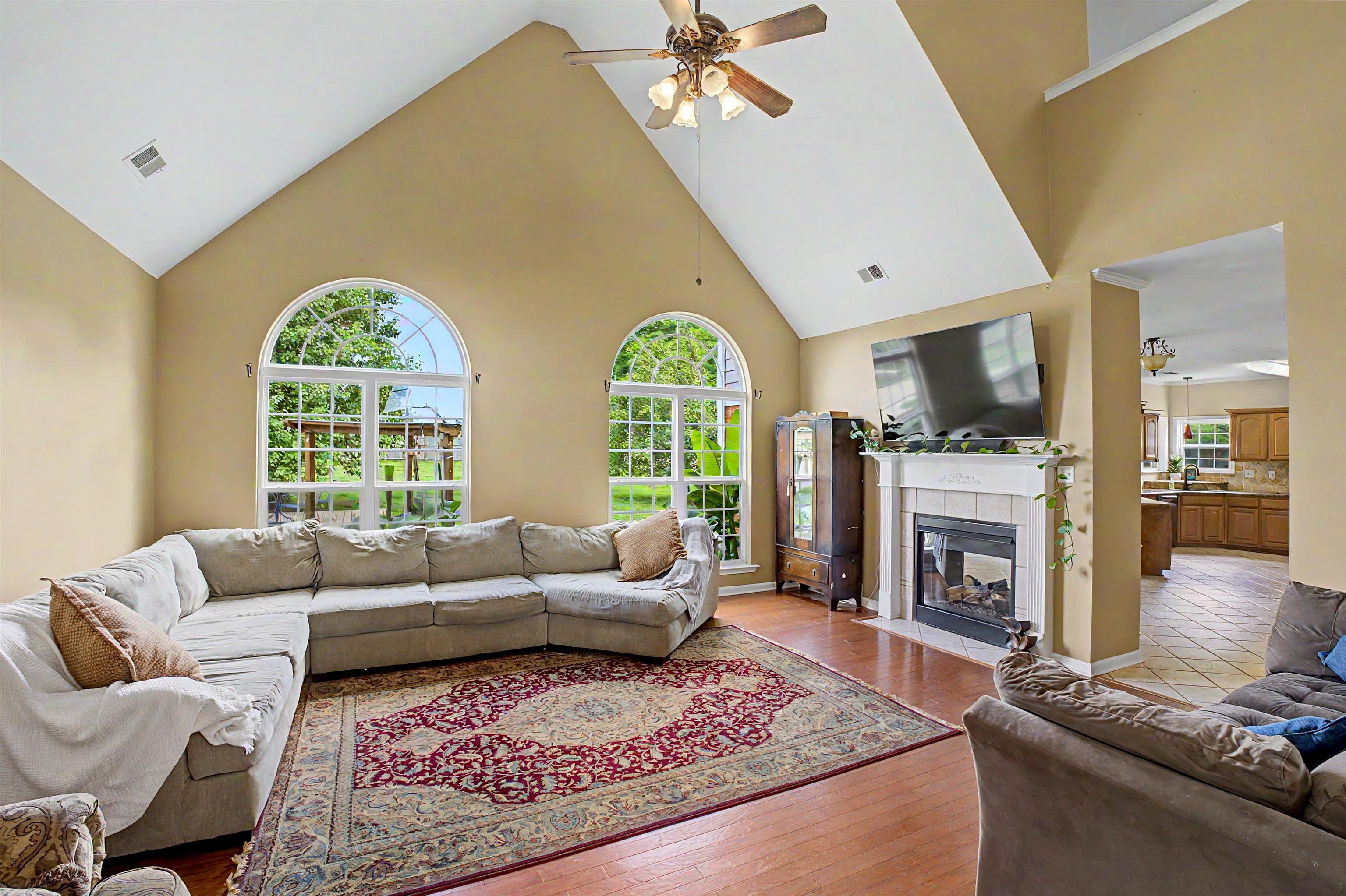 134 Rembert Drive Atoka, TN 38004 - Photo 9 of 38 Spacious living room featuring vaulted ceilings, two arched windows, wood-finish flooring, and a fireplace with a decorative mantel