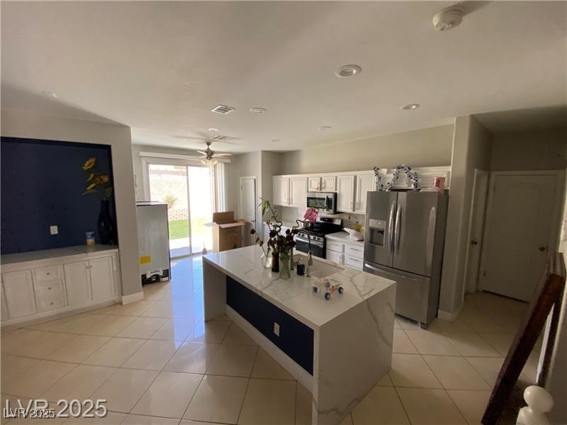 1154 Warm Sun Court Las Vegas, NV 89110 - Photo 18 of 19 Kitchen with stainless steel appliances, white cabinetry, light tile patterned flooring, a center island, and light stone countertops