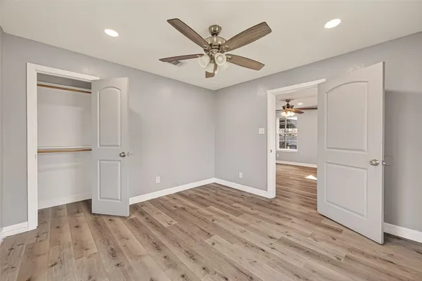 an empty room with wooden floor a ceiling fan and windows