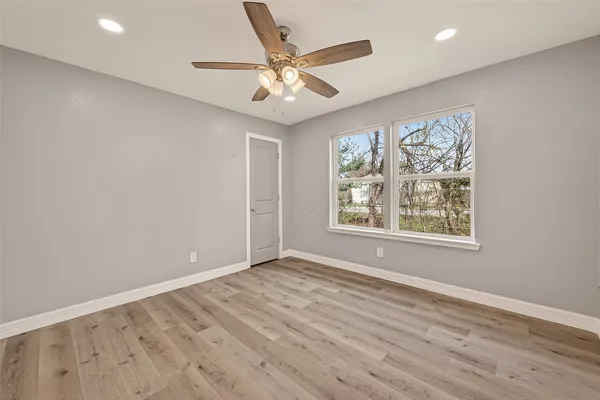 an empty room with wooden floor chandelier fan and windows