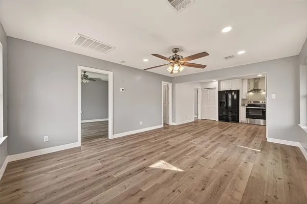 a view of an empty room with wooden floor and a ceiling fan