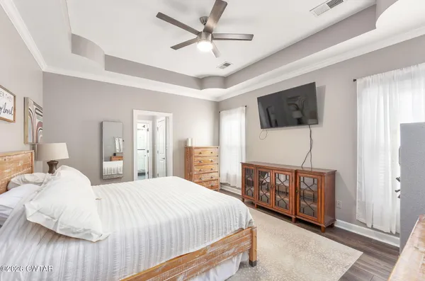 a bedroom with a large bed a flat tv screen on dresser and a wooden floor