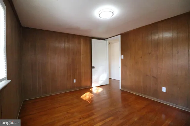 an empty room with wooden floor and windows with curtains