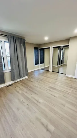 a view of an empty room with window and wooden floor
