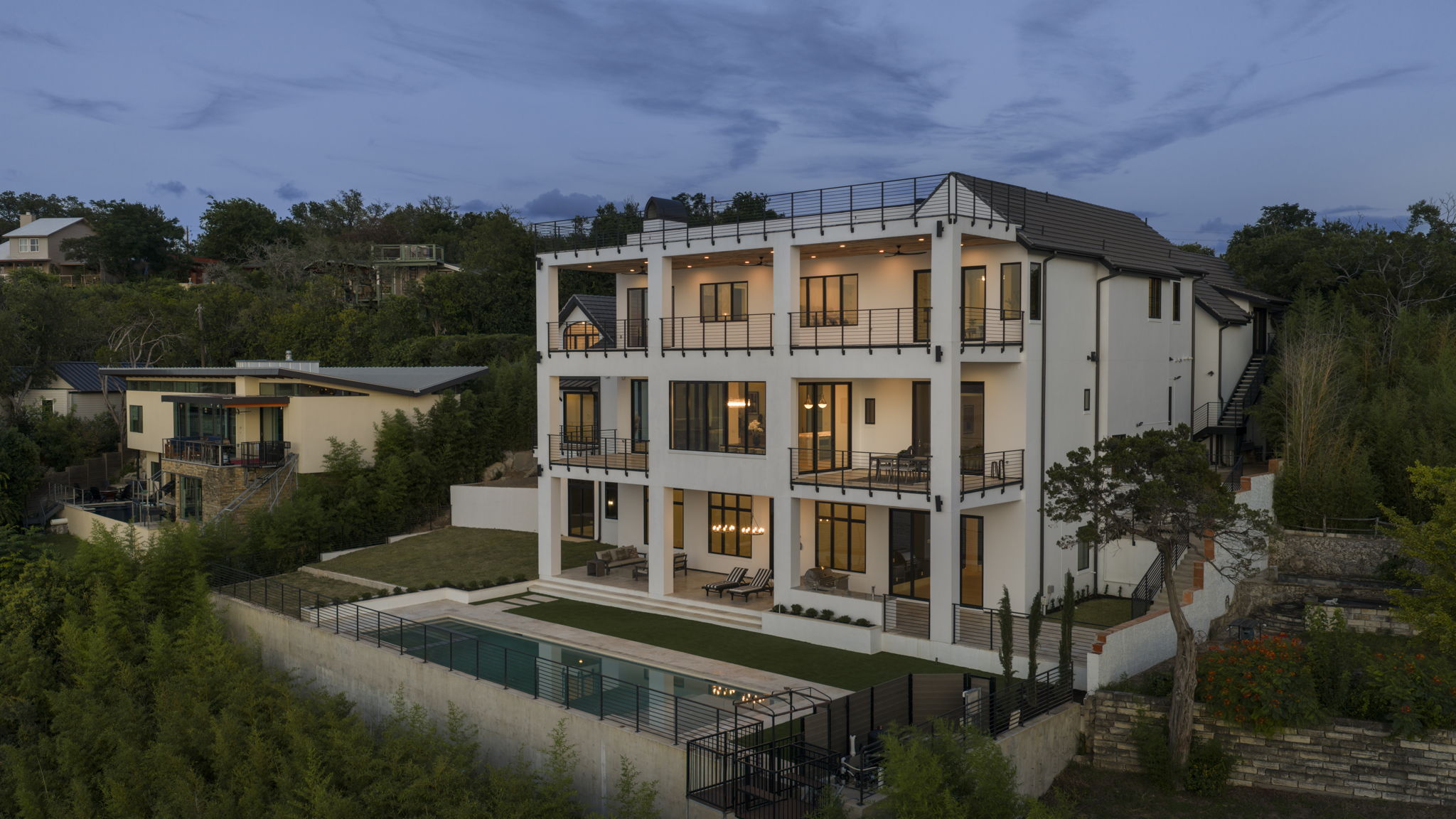Multi-story architecture with tiered balconies overlooks a secluded backyard oasis and sparkling pool.