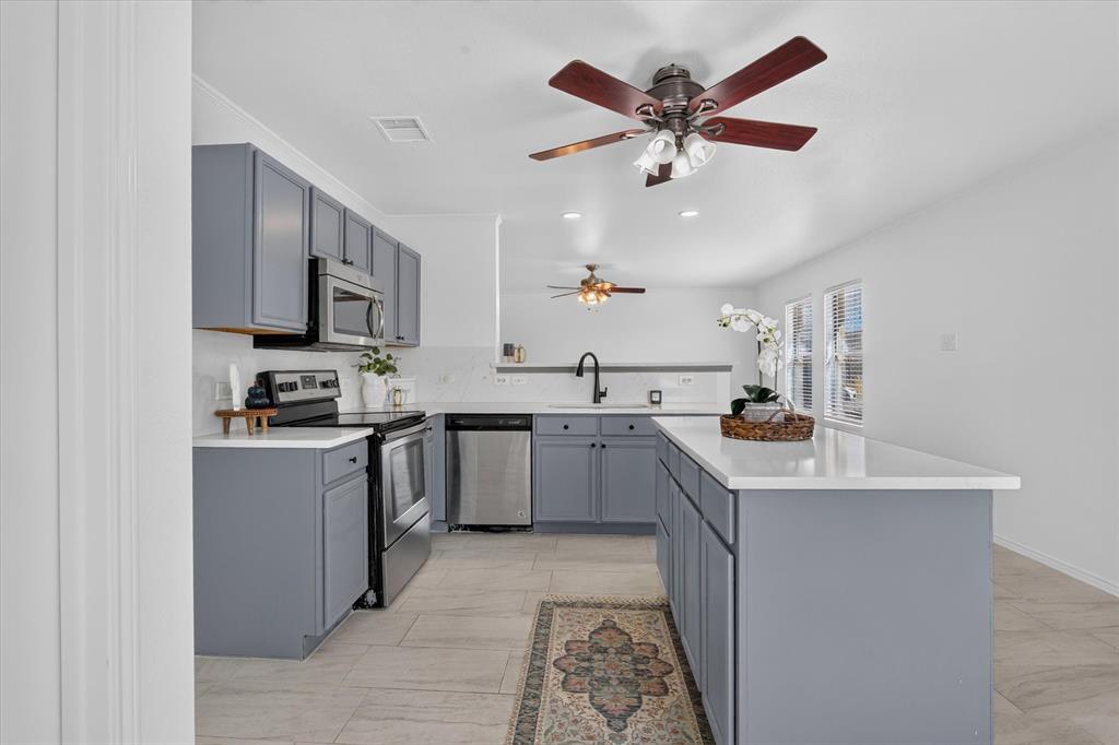 Open concept kitchen featuring gray cabinetry, stainless steel appliances, and a central island with countertop seating