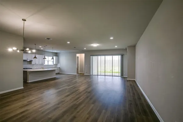a view of an empty room with kitchen and window