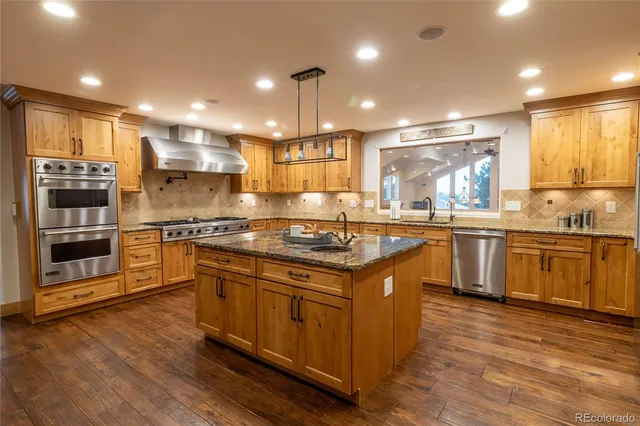 a kitchen with stainless steel appliances granite countertop a stove a sink a refrigerator and white cabinets with wooden floor