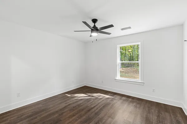 an empty room with wooden floor ceiling fan and windows