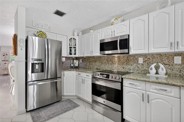 a kitchen with stainless steel appliances granite countertop white cabinets a refrigerator a stove a sink and dishwasher
