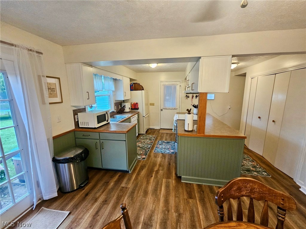 6620 West Lake Road Vermilion, OH 44089 - Photo 14 of 34 Kitchen featuring wood-finish flooring, white upper cabinetry, sage green lower cabinetry, and a peninsula with a breakfast bar