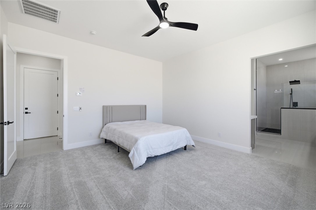 5910 East Kellogg Road Pahrump, NV 89061 - Photo 32 of 58 A well-lit bedroom with soft carpeting and a modern ceiling fan, offering direct access to a spacious walk-in shower.