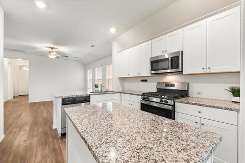 a kitchen with stainless steel appliances kitchen island granite countertop a stove top oven a sink a counter space and cabinets