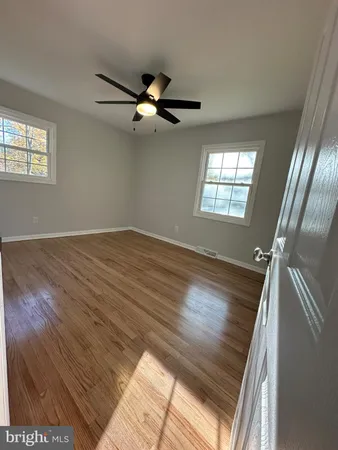 an empty room with wooden floor fan and windows