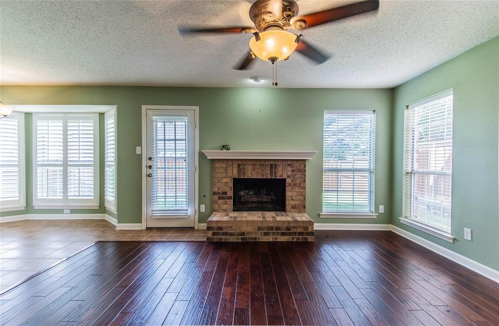 4117 Oxlea Drive Plano, TX 75024 - Photo 10 of 17 an empty room with wooden floor a fireplace a ceiling fan and windows