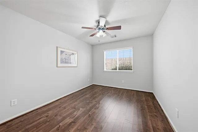 an empty room with wooden floor ceiling fan and windows