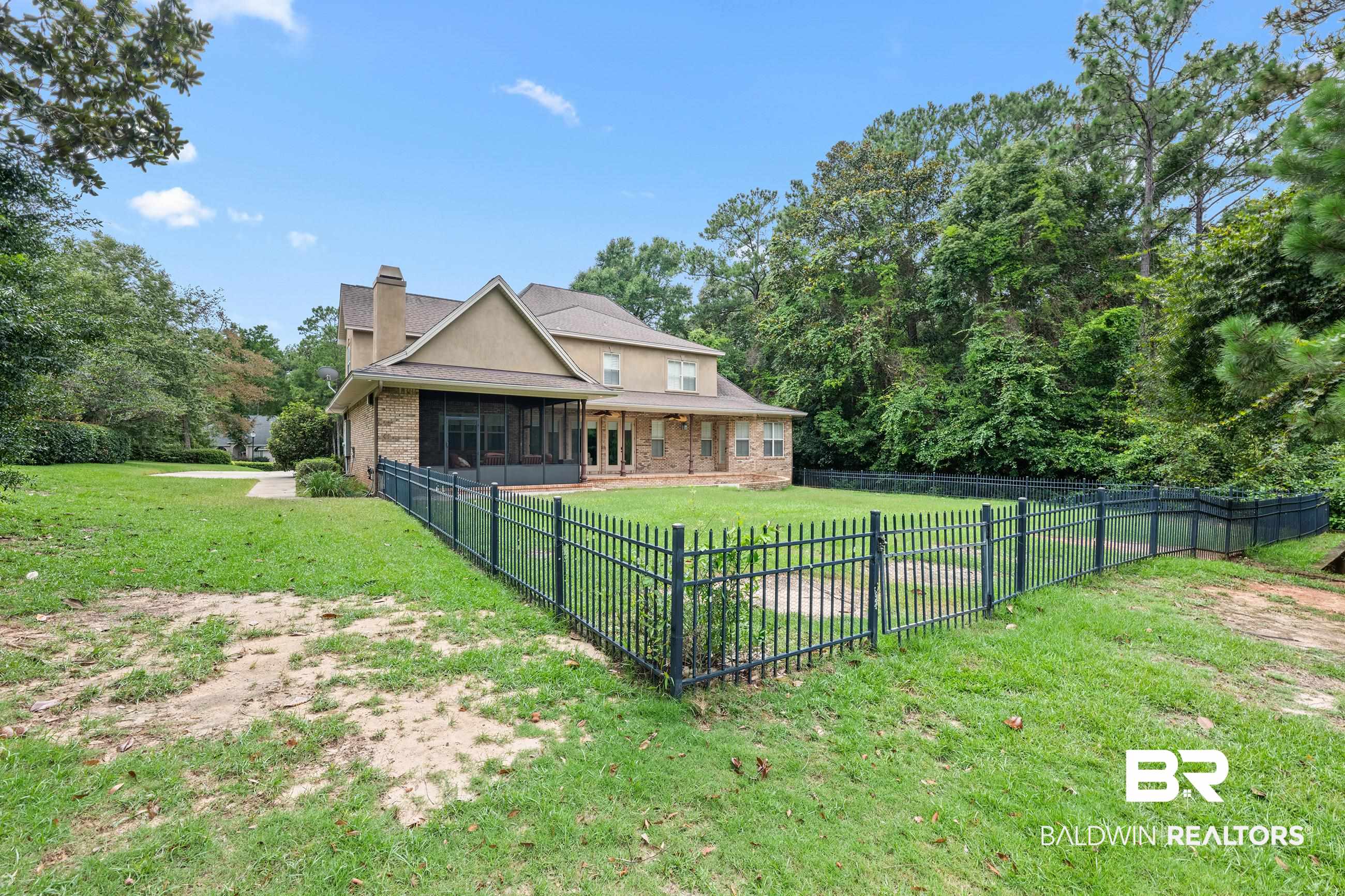 30463 Dolive Ridge Daphne, AL 36527 - Photo 14 of 58 Expansive backyard featuring a black metal fence, mature trees, a screened porch, and a brick and stucco exterior with a prominent chimney