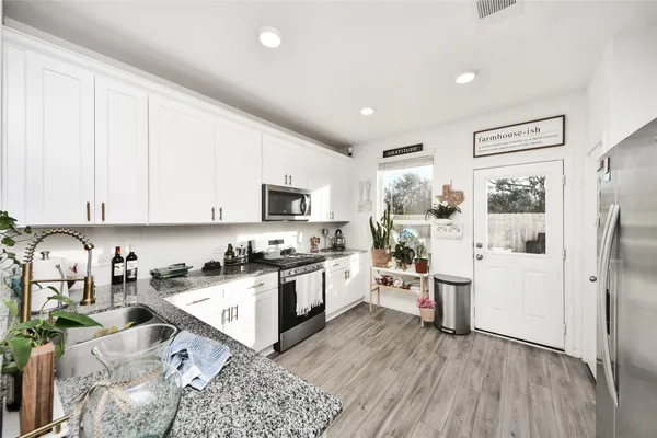 a kitchen with stainless steel appliances granite countertop a stove top oven a sink dishwasher and a refrigerator with wooden floor