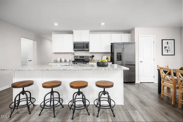a kitchen with stainless steel appliances granite countertop a stove a refrigerator a microwave a dining table and chairs cabinets with wooden floor