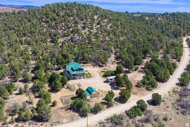 75 Wray Mesa Road La Sal, UT 84530 - Photo 6 of 59 Property featuring a multi-story residence with a green roof, attached garage, and a separate outbuilding, all set within a natural, treed landscape with a visible unpaved road