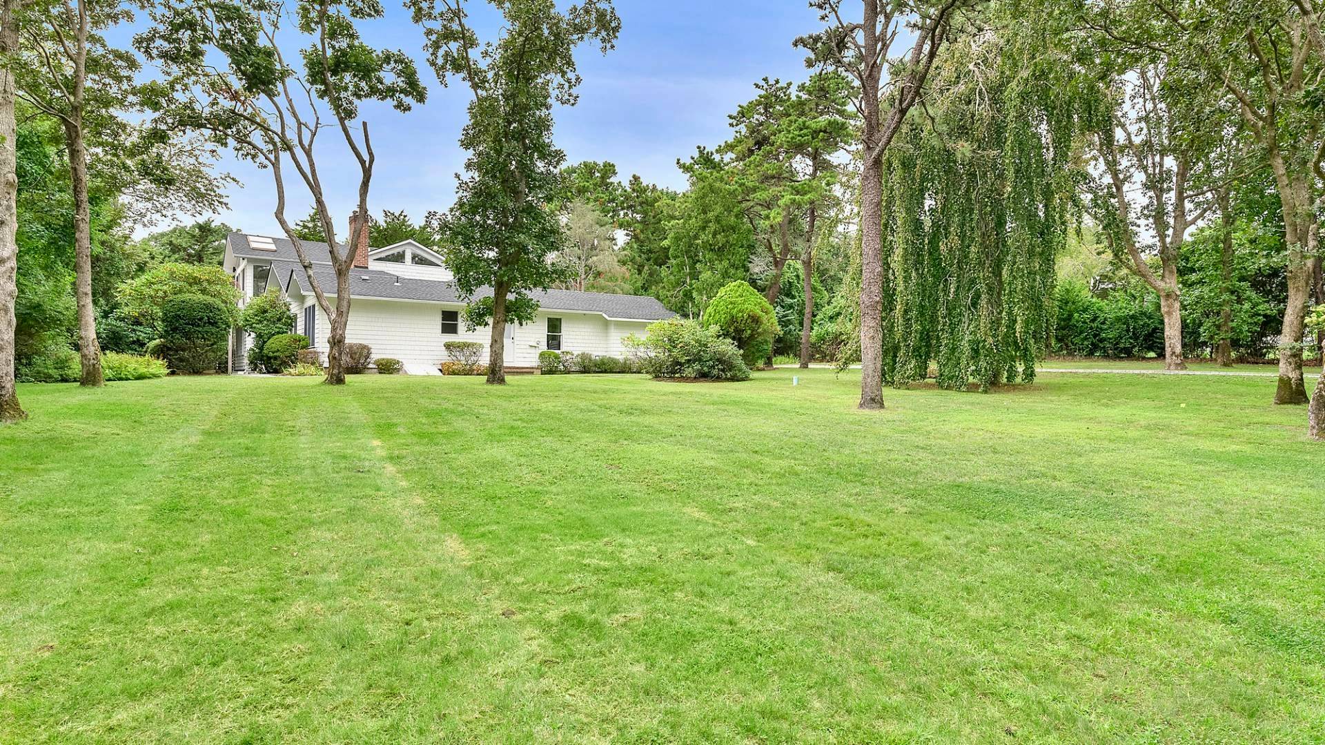 a view of white house with a big yard and large trees