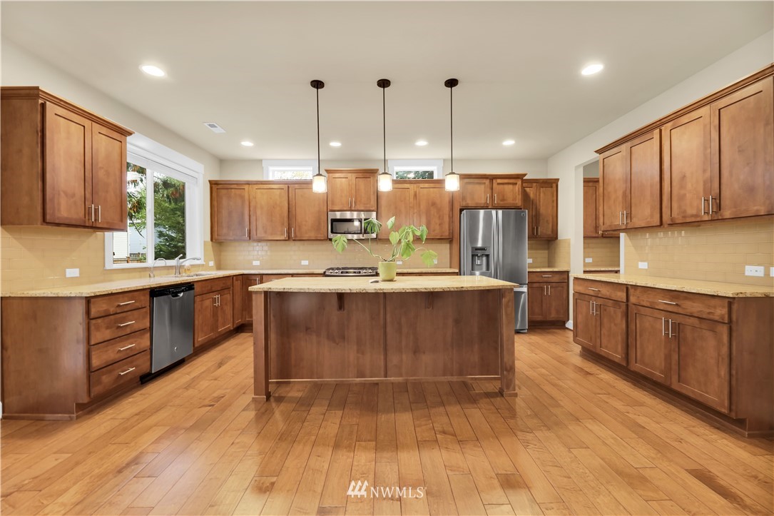 6117 Northeast 1st Street Renton, WA 98059 - Photo 8 of 39 a large kitchen with kitchen island granite countertop a stove a sink a refrigerator and cabinets
