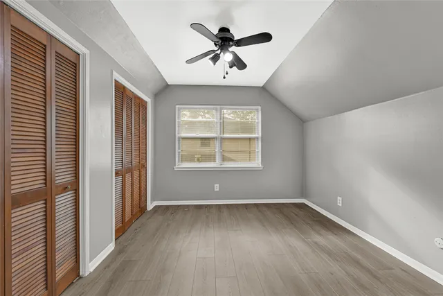 an empty room with wooden floor chandelier fan and windows