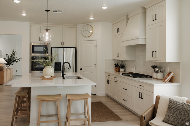 629 Spring Lily Drive St. George, UT 84790 - Photo 8 of 50 Contemporary kitchen featuring a large central island with an undermount sink, stainless steel appliances, white subway tile backsplash, and light-toned cabinetry with matte black hardware
