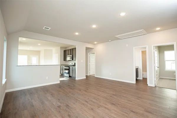a view of empty room with wooden floor and kitchen