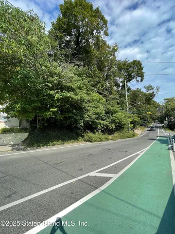 a view of a street with a yard and large trees