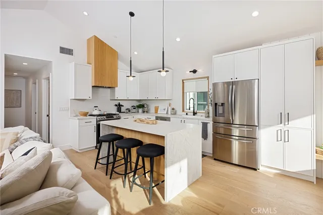 a kitchen with stainless steel appliances kitchen island granite countertop a refrigerator a sink a stove and white cabinets with wooden floor