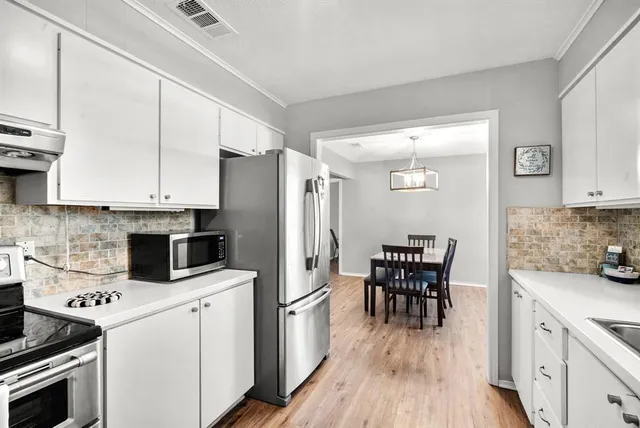 a kitchen with stainless steel appliances a stove a sink dishwasher a refrigerator white cabinets with wooden floor