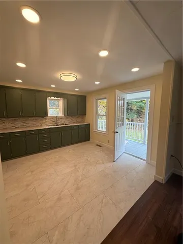 a view of an empty room with wooden floor and a kitchen