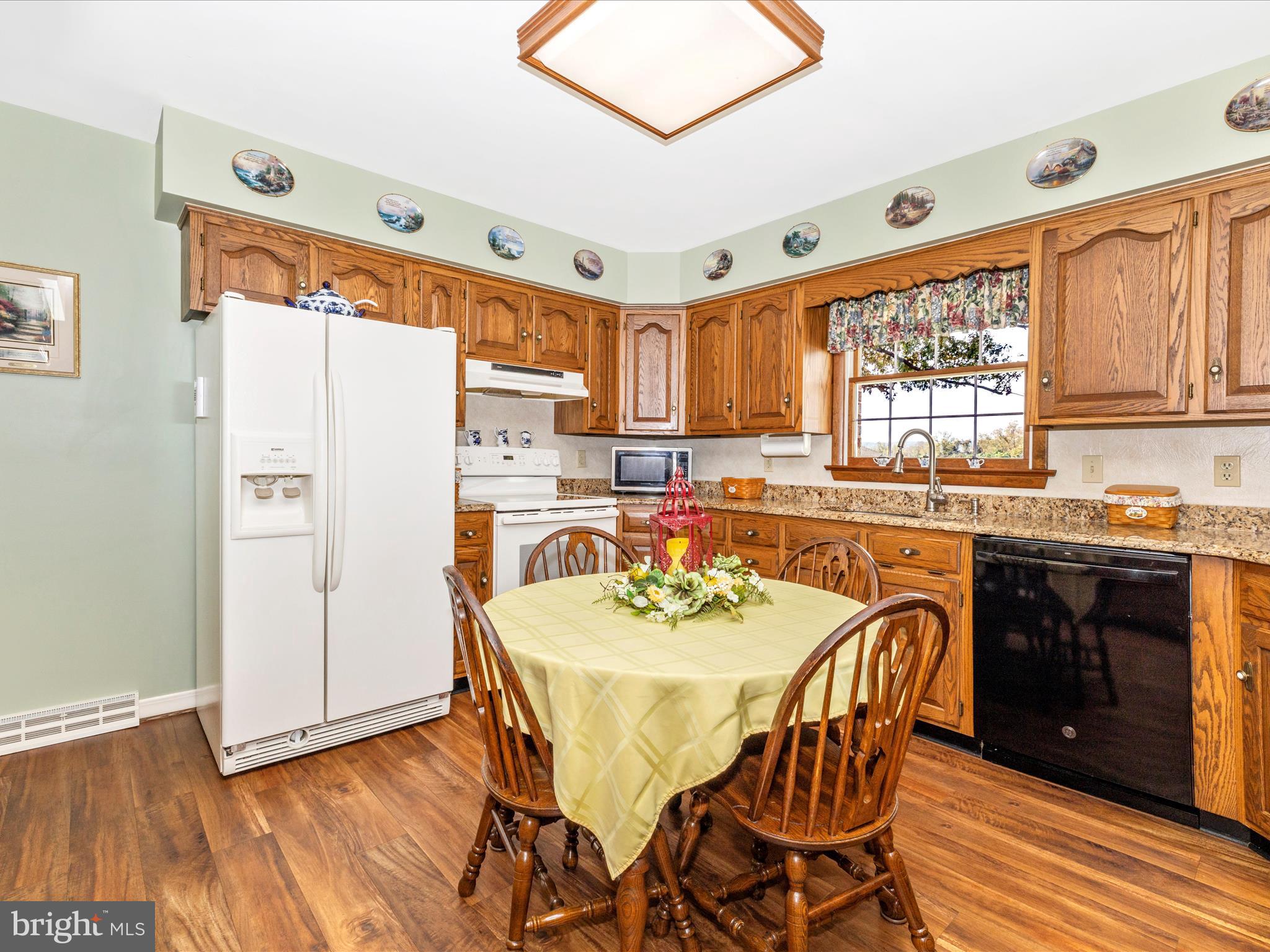 12720 Spickler Road Clear Spring, MD 21722 - Photo 14 of 57 a kitchen with stainless steel appliances granite countertop a stove a refrigerator a sink a dining table and chairs with wooden floor