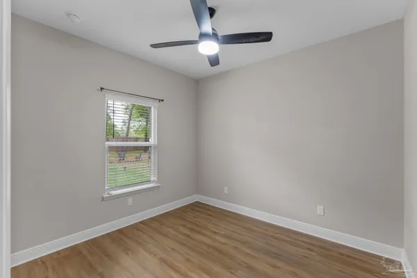 an empty room with wooden floor ceiling fan and windows