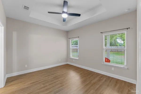 an empty room with wooden floor ceiling fan and windows