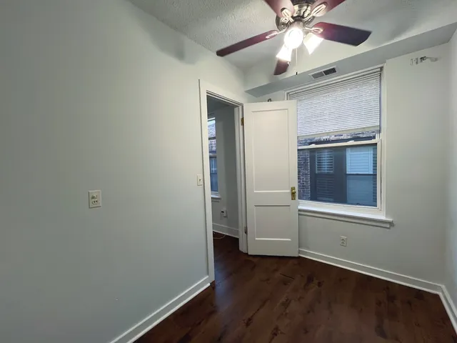 an empty room with wooden floor chandelier fan and windows