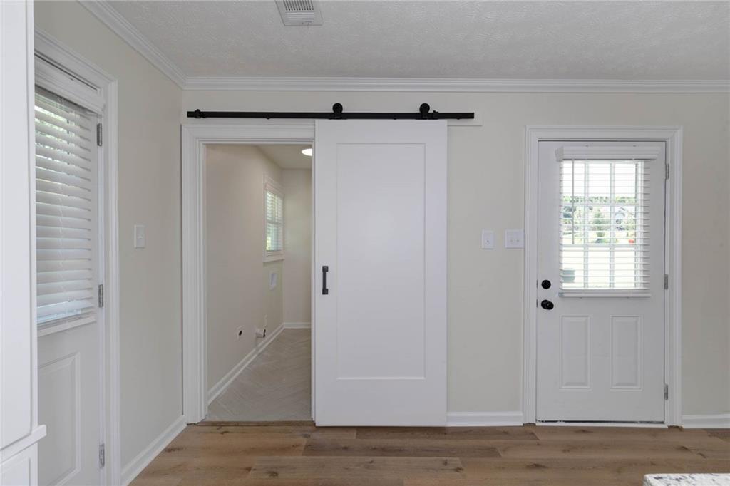 2899 Lamb Road Smiths Station, AL 36877 - Photo 11 of 26 Wood-finish flooring with white baseboards, a white barn door on a black track, and a white exterior door with an inset window