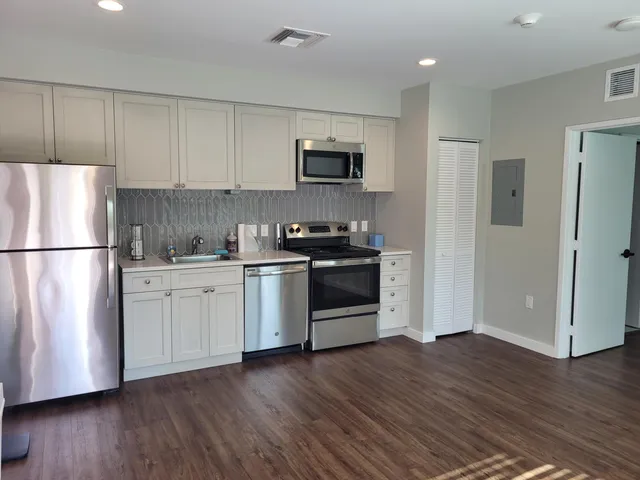 a kitchen with stainless steel appliances granite countertop a refrigerator stove a sink and white cabinets with wooden floors