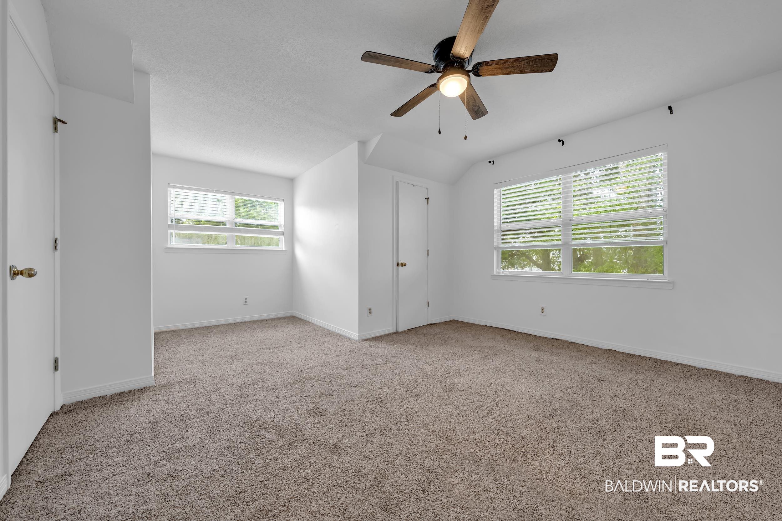 17488 Pandion Ridge, Unit A1 Fairhope, AL 36532 - Photo 15 of 18 Carpeted room featuring a ceiling fan with light fixture, multiple windows with blinds, white walls, and a white door with a brass-finish doorknob