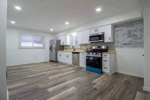a kitchen with stainless steel appliances granite countertop a stove top oven a sink dishwasher and a refrigerator with wooden floor