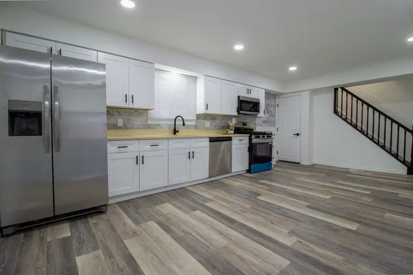 a kitchen with stainless steel appliances granite countertop a refrigerator a sink dishwasher a stove and white cabinets with wooden floor