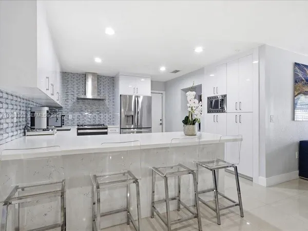 a kitchen with stainless steel appliances kitchen island granite countertop a stove a sink a refrigerator and white cabinets with wooden floor