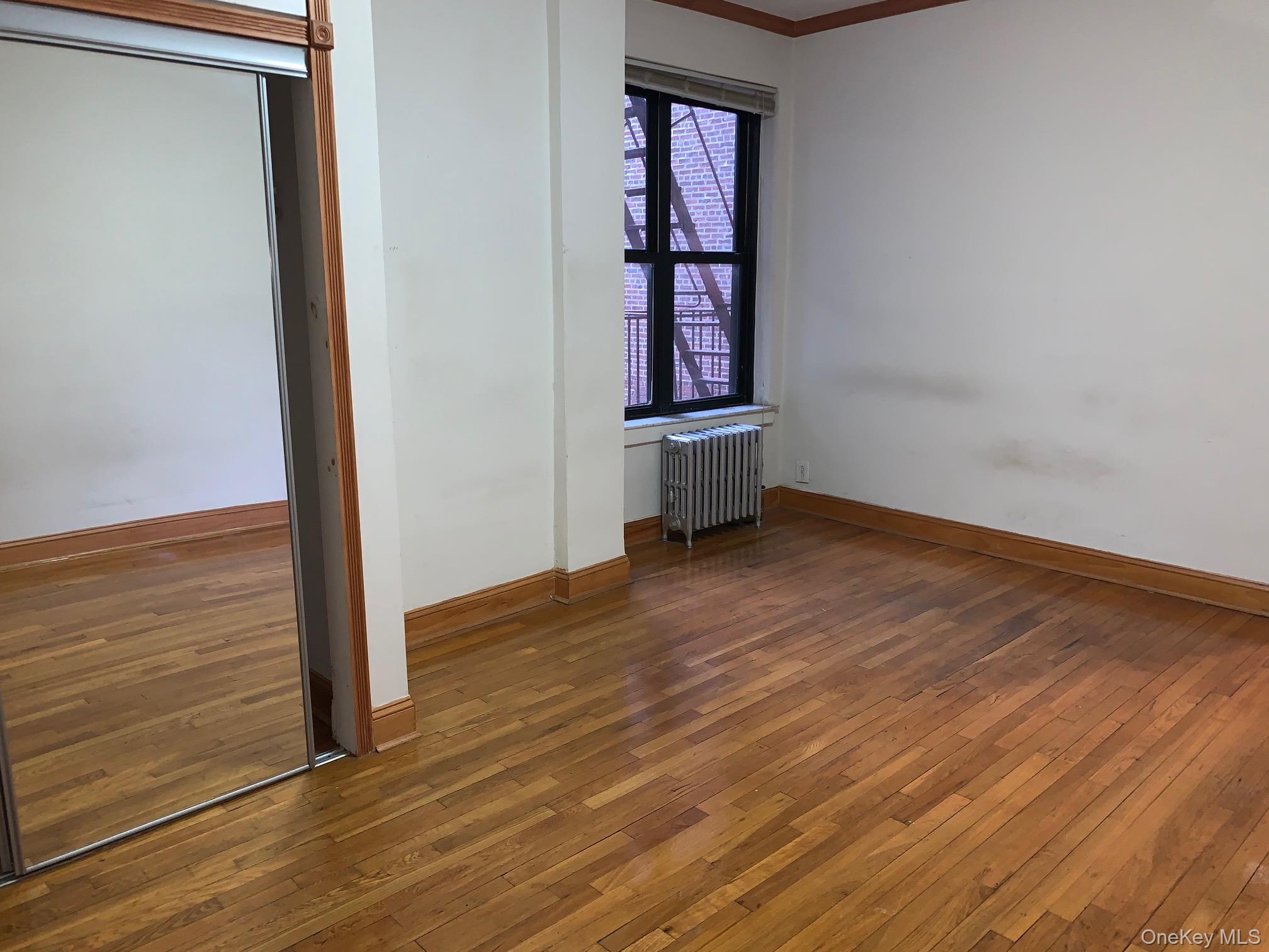 43-33 48th Street, Unit 4E Queens, NY 11104 - Photo 14 of 16 an empty room with wooden floor and windows