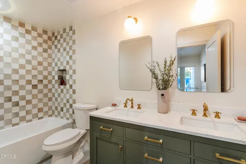 a bathroom with a granite countertop toilet a sink a mirror a lamp and shower