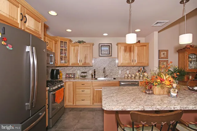 a kitchen with stainless steel appliances granite countertop a sink a stove a refrigerator and chairs