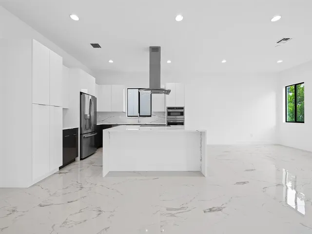 a large white kitchen with a sink a counter top space and stainless steel appliances
