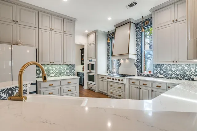 a large white kitchen with stainless steel appliances a stove a sink a refrigerator and white cabinets with wooden floor